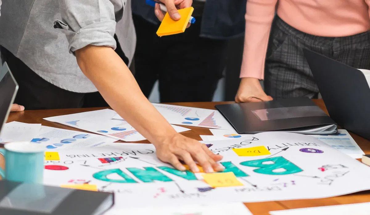 Marketing team brainstorming campaign creative across documents and a brand strategy table